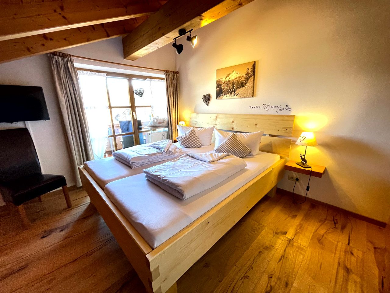 Gemütlichdes Schlafzimmer mit einem Holzbett, das auf einem Holzfussboden steht mit einem Bild mit Bergmotiv an der Wand.